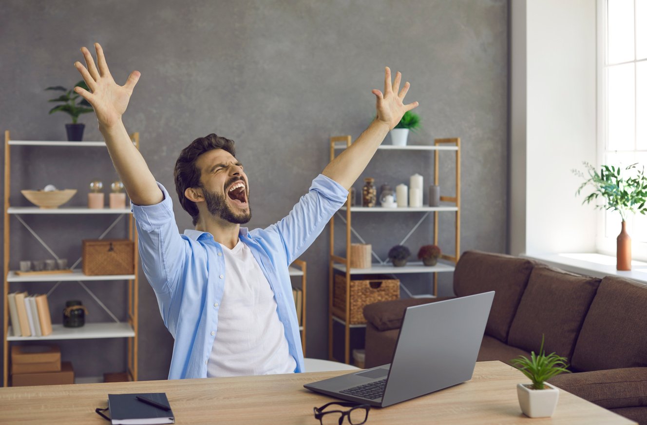 Happy Excited Young Man Screaming Sitting at His Working Desk with Laptop Computer